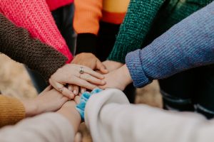 many people with brightly colored sweaters, with their arms in the center to begin a teamwork cheer. 
