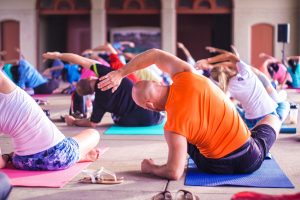 group workout class performing right sided overhead stretch in seated, everyone is wearing vibrant colors