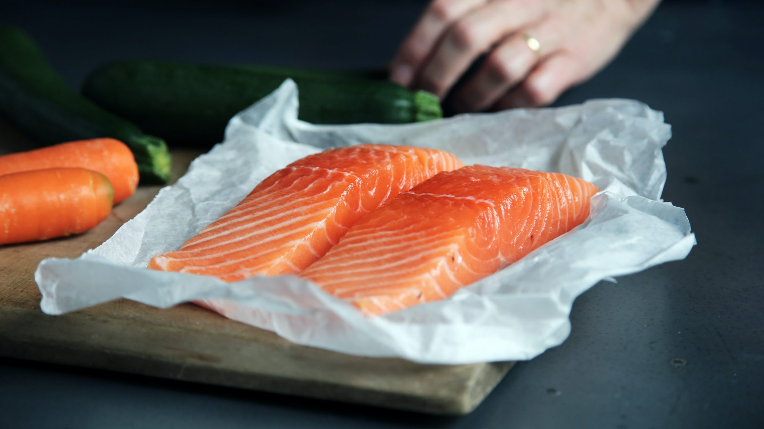 Photo of 2 salmon fillets on foil, with a mans hand in the background getting ready to cook them.