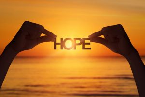 two hands holding the word hope in front of a sunset