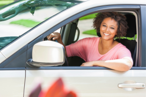 darker skinned woman with a pink shirt smiling from inside her white car, she has recovered from being dizzy while driving